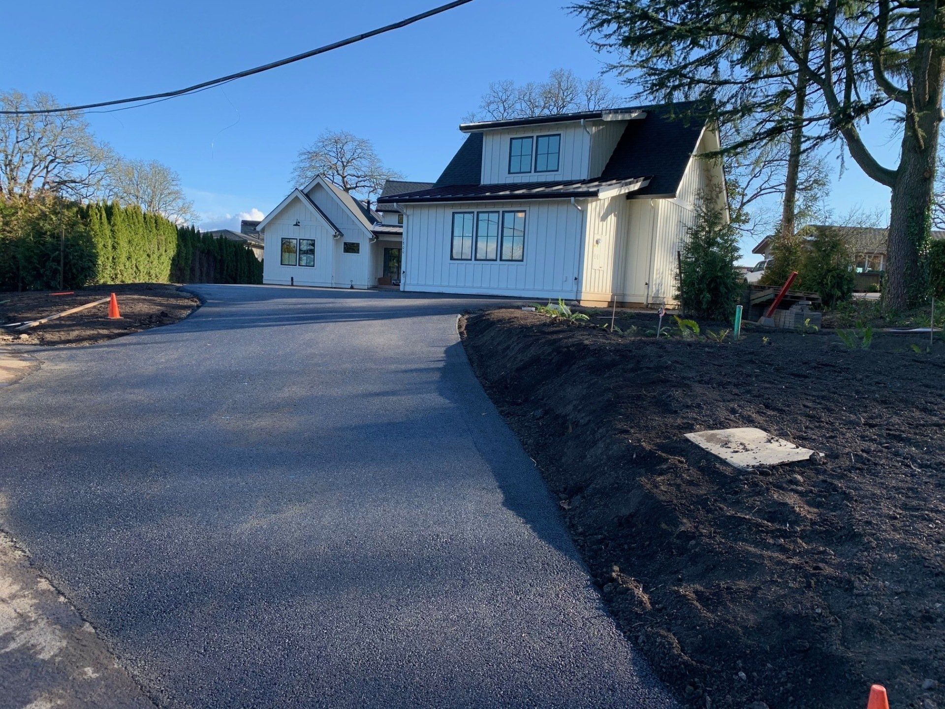 Asphalt driveway leading to white houses with black roofs and landscaping.