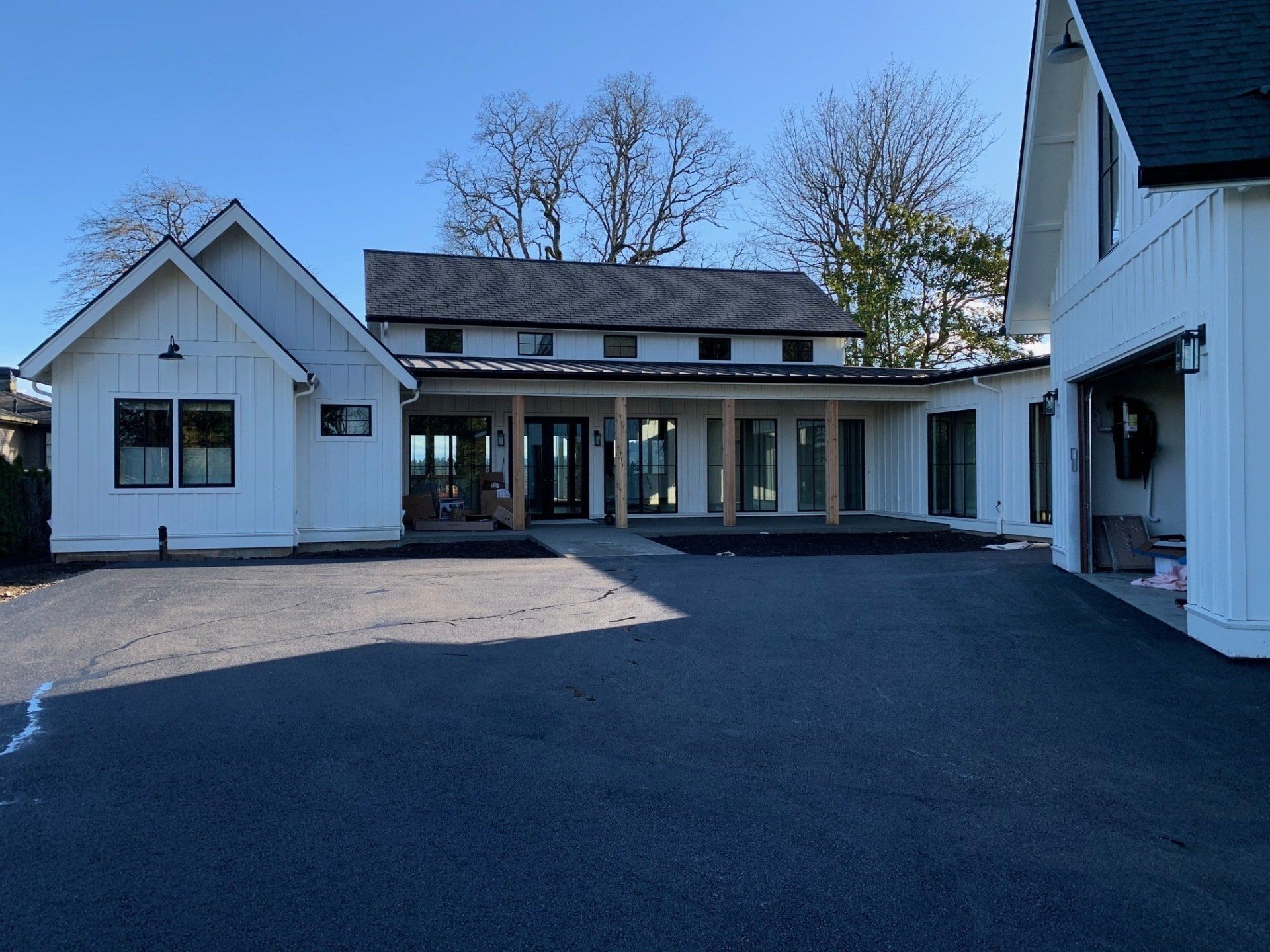 White farmhouse with black trim, asphalt driveway, and porch with wooden columns.