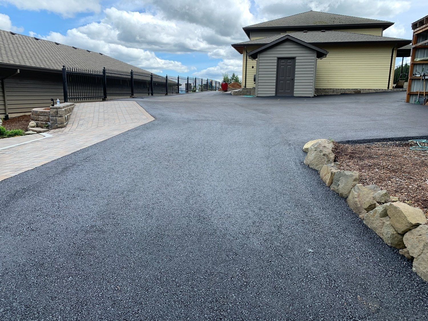 Gravel driveway leading to buildings with a small shed. Cloudy sky overhead.