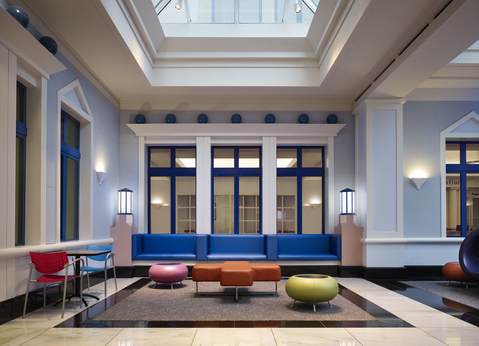 Interior of a building with a blue and orange seating area, windows, and colorful chairs. Skylight above.