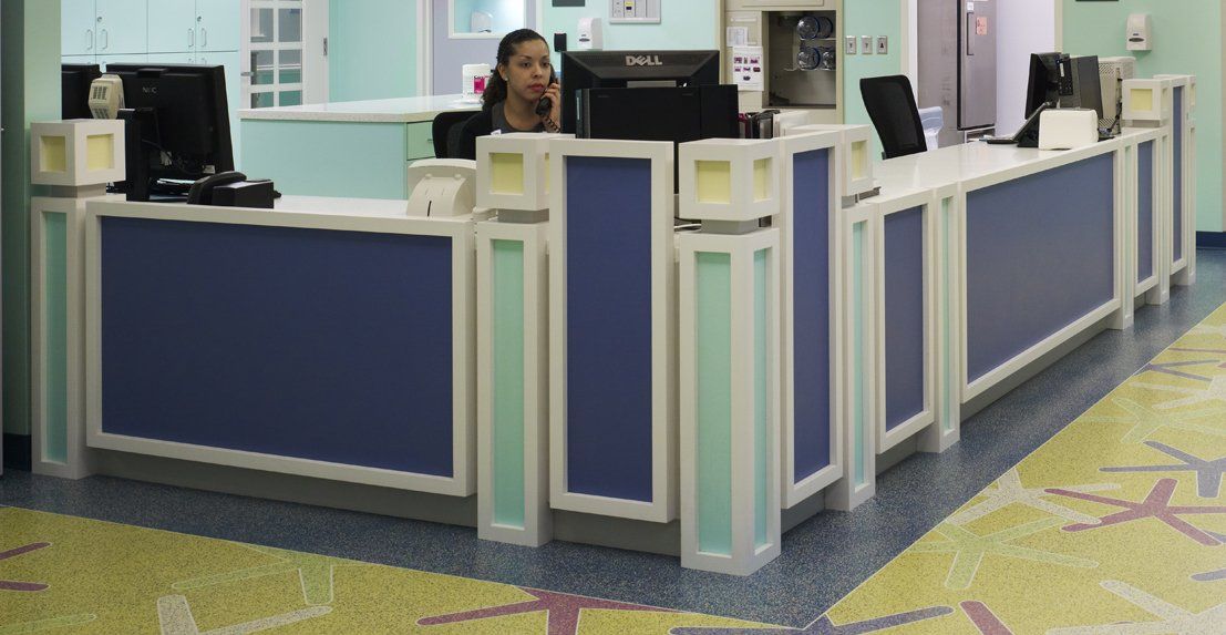 Reception desk with a person on the phone; blue and white decor with a yellow and green carpet.