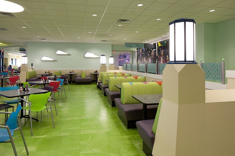 Brightly colored cafeteria with green floors, booths, and tables.  Shoes are mounted on the wall, and a light fixture is in the foreground.