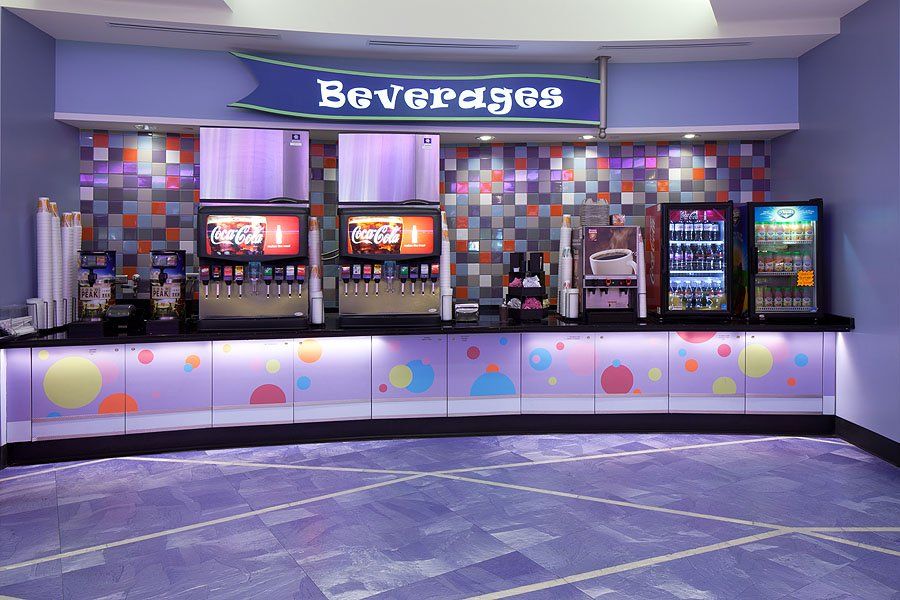 Beverage counter in a brightly lit space, featuring soda dispensers, a refrigerated display, and a colorful decorative front panel.