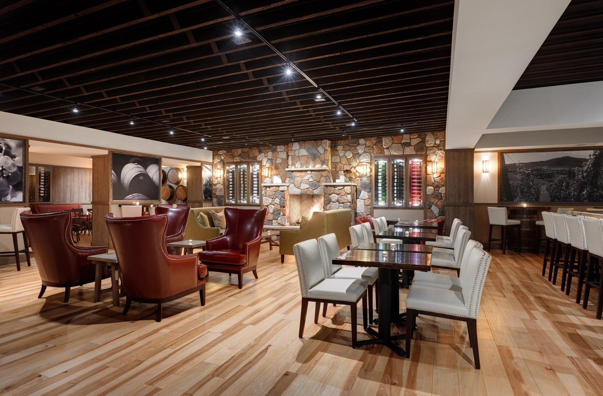 Upscale restaurant interior with wooden floor, leather armchairs, dining tables, and a stone wall with wine display.