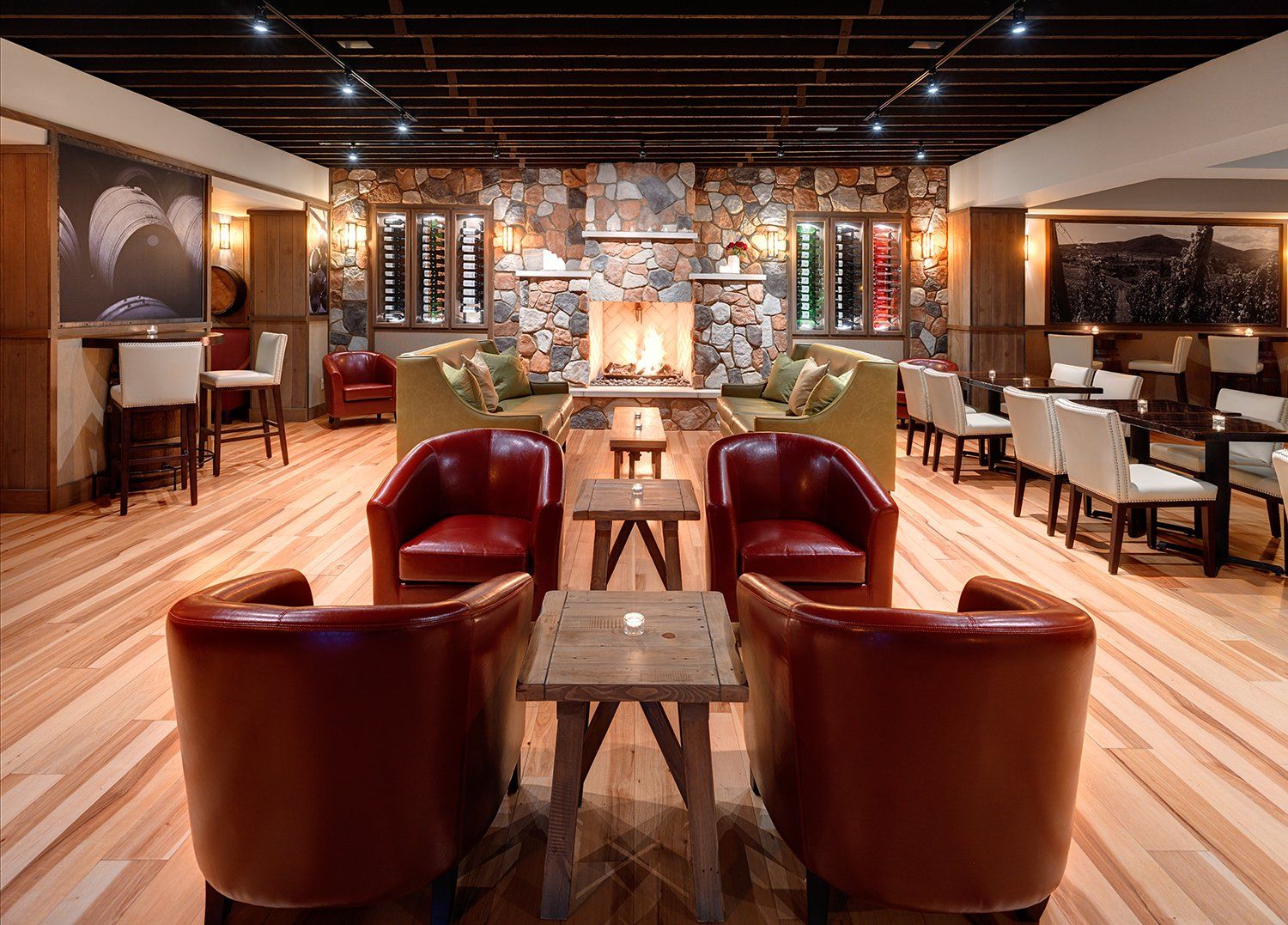 Cozy bar lounge with fireplace, red and green seating, wooden tables, and wine displays. Well-lit with a warm, inviting atmosphere.