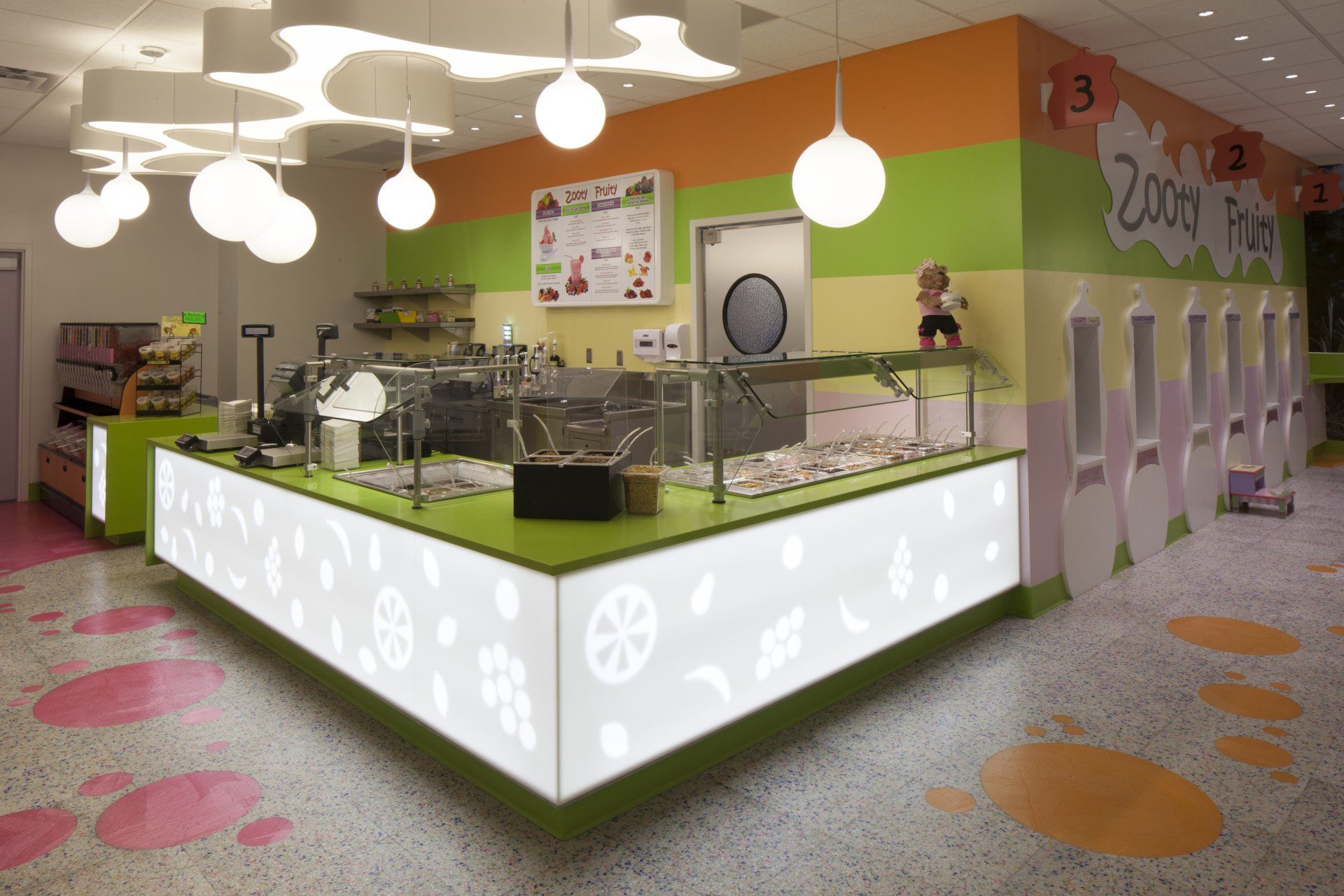 Brightly lit kids' food shop with a counter displaying food. The walls are striped green, orange, and pink, and the floor is speckled.