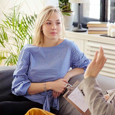 Une femme est assise sur un canapé et parle à un homme tout en tenant un presse-papiers.