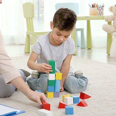 Un jeune garçon est assis par terre et joue avec des blocs de bois.