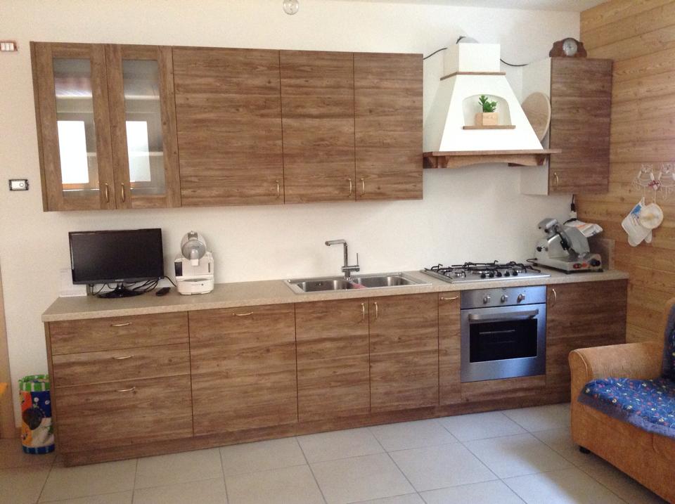 Cucina moderna con mobili in legno, pavimento piastrellato, piano cottura, lavello e un piccolo elettrodomestico da banco.