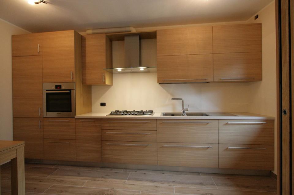 Cucina moderna in legno con forno a incasso, piano cottura, mobili e lavello, illuminata da una luce calda.