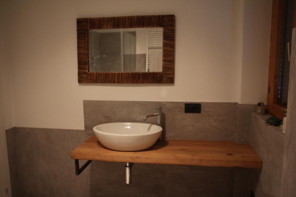 Mobiletto da bagno di piccole dimensioni con lavabo a ciotola bianco, piano in legno e specchio a parete.