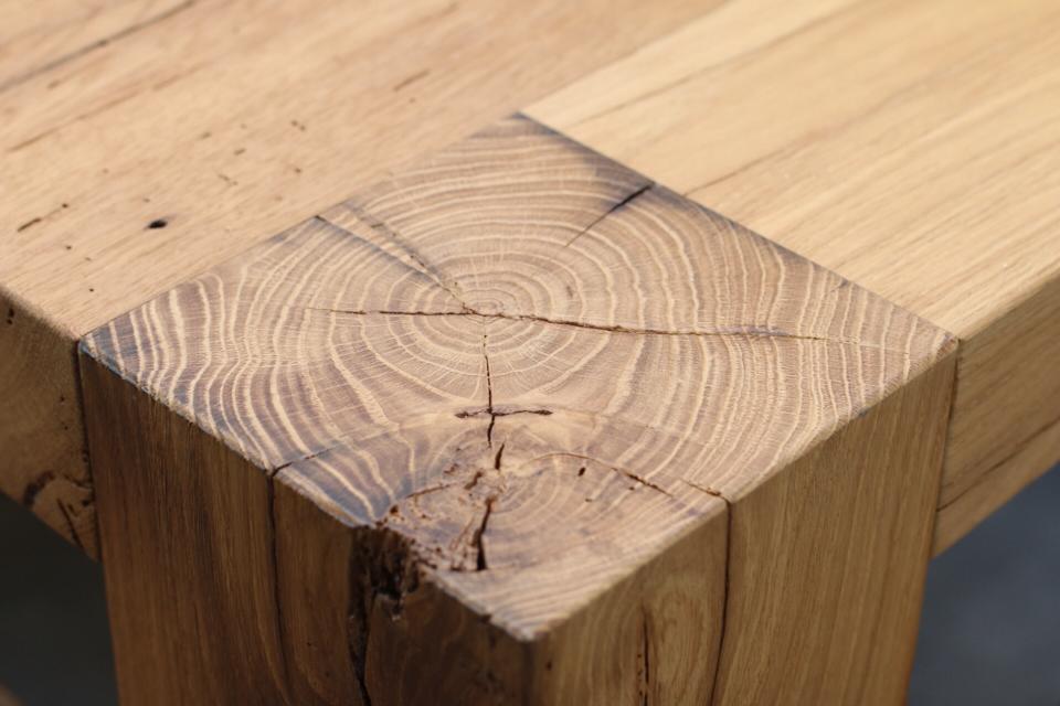 Primo piano di un angolo di un tavolo di legno incrinato, con venature di testa visibili e una giunzione danneggiata.