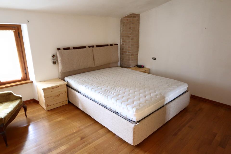 Camera degli ospiti con letto grande, pavimento in legno, finestra e camino in mattoni.
