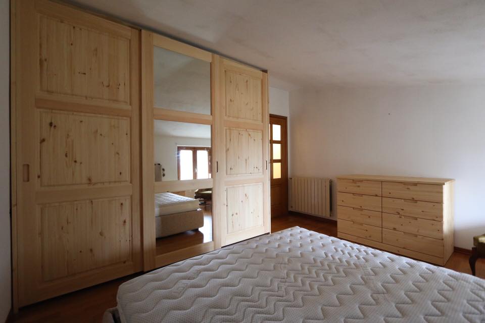 Camera da letto con armadi in legno, cassettiera e letto in una stanza luminosa e arredata in modo essenziale.