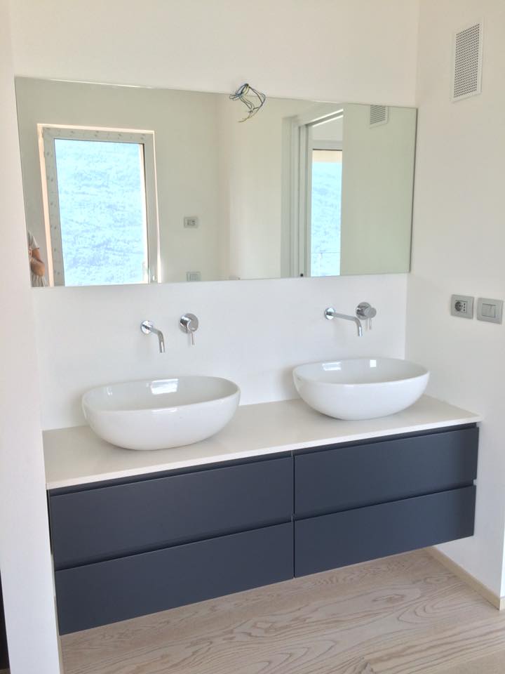 Mobile bagno moderno con due lavabi a ciotola bianchi, cassetti scuri e specchio sopra.