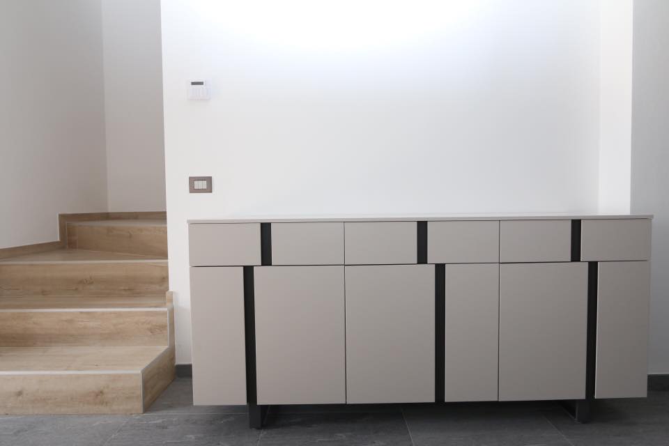 Mobiletto moderno beige con gambe nere accanto a una scala in legno in una stanza minimalista