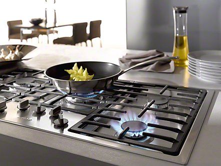 Cucina moderna con fornello a gas, padella, fiamme blu e tavolo da pranzo sullo sfondo.