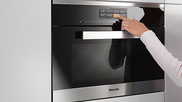 Una mano si allunga per premere i comandi di un forno a incasso in acciaio inossidabile.