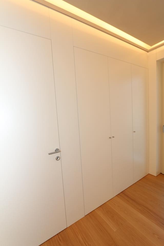 Ante di armadi a muro bianche in un corridoio minimalista con pavimento in legno caldo e illuminazione a soffitto.