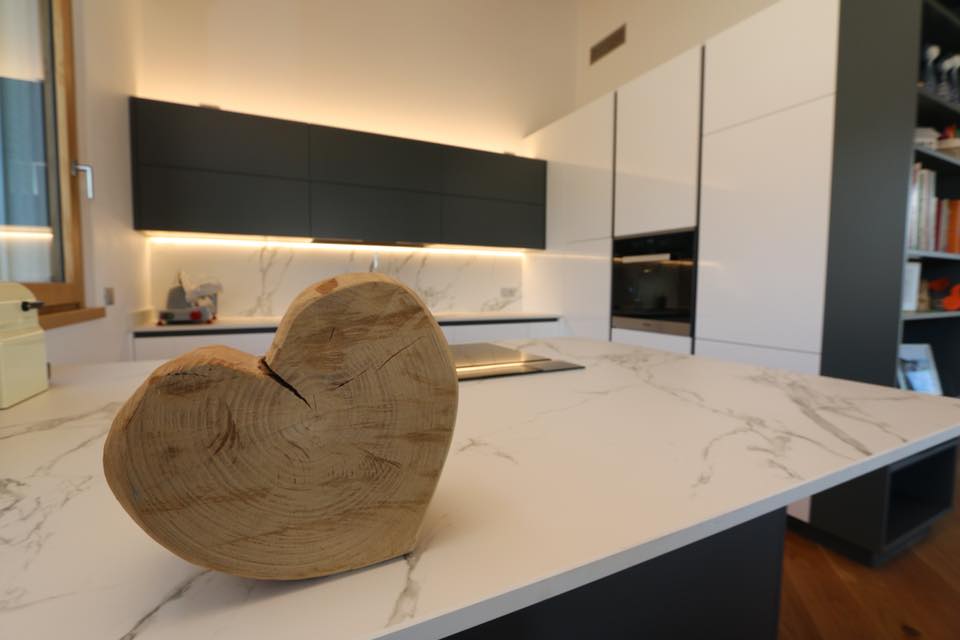 Cucina moderna con isola in marmo, illuminazione sottopensile calda e un centrotavola a forma di cuore in legno intagliato.