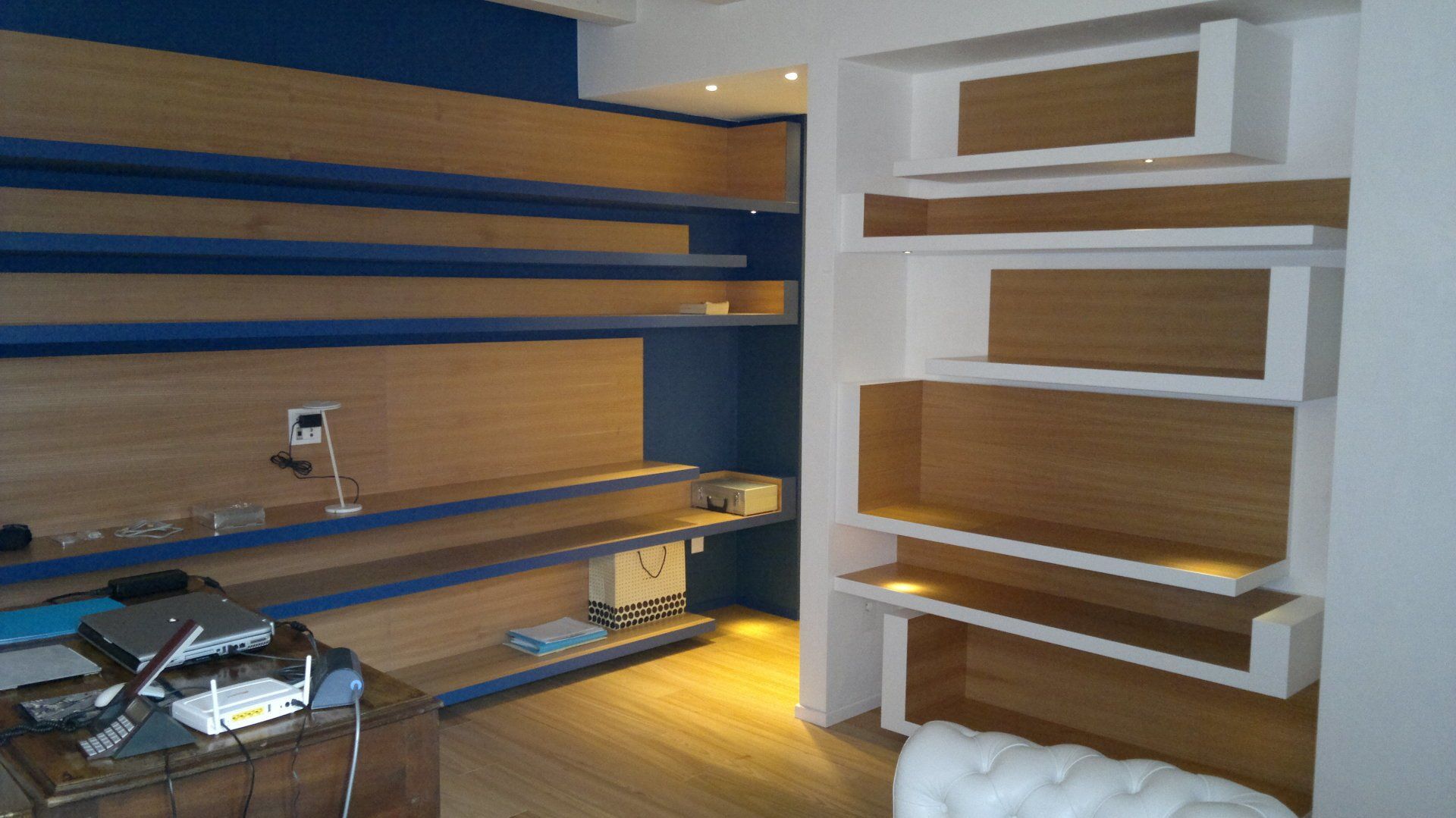 Stanza moderna vuota con scaffali blu e in legno, una scrivania e luci a incasso calde.