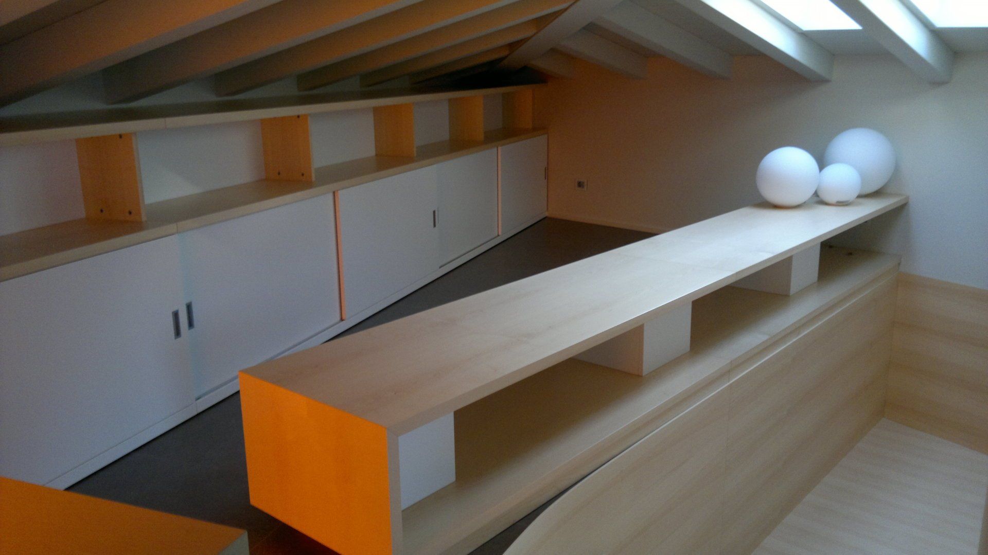 Soffitta bassa con armadietti a muro bianchi, una panca in legno e due sfere bianche sulla mensola.