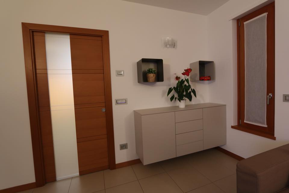 Corridoio moderno con porte in legno, mobile bianco, mensole a muro e un vaso di fiori.