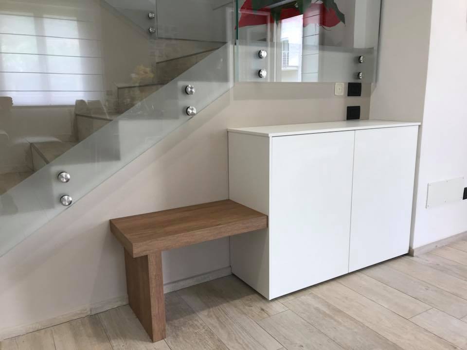 Mobile bianco e gradino in legno sotto una scala in vetro in un interno di casa moderna.