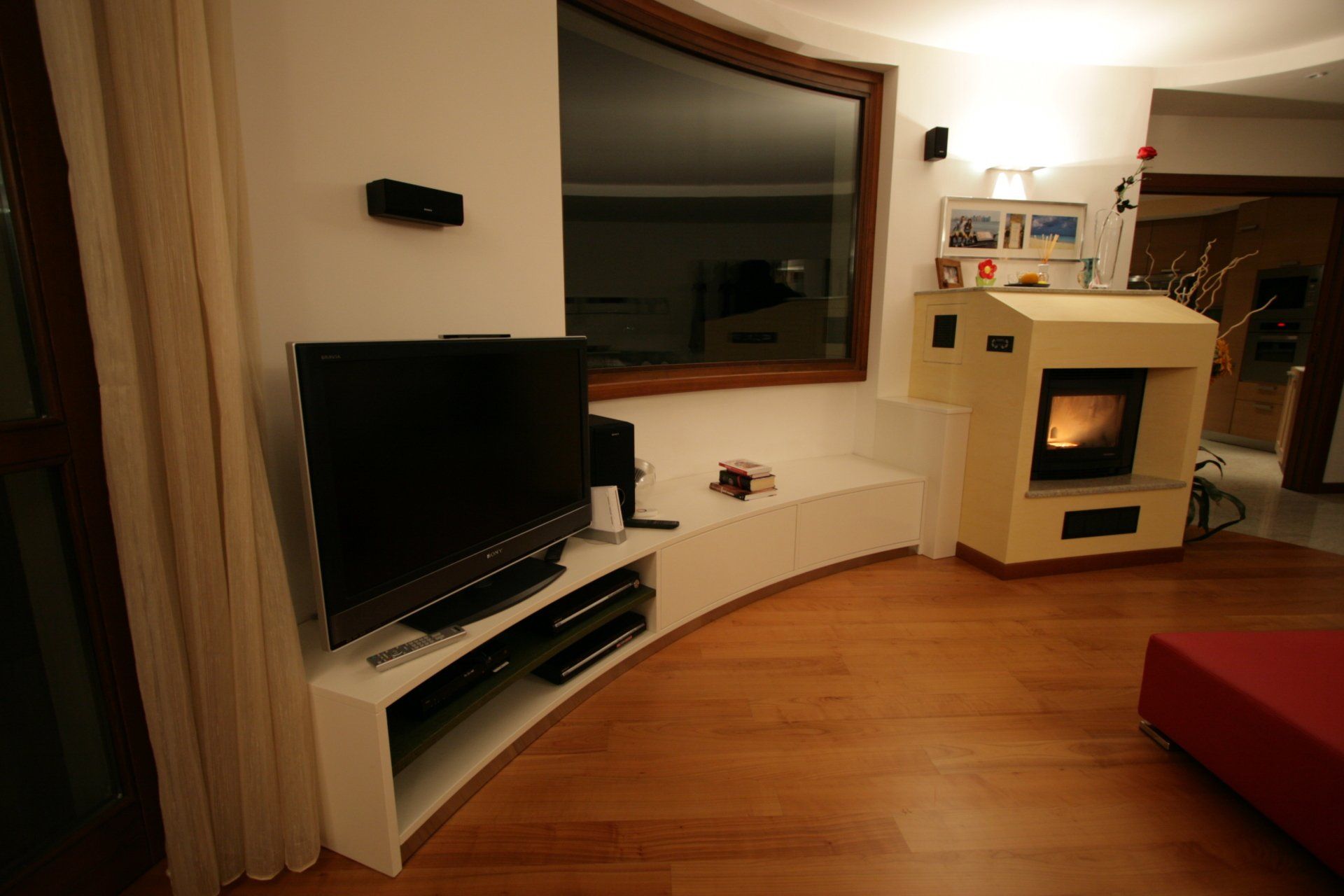 Soggiorno moderno con TV, consolle bianca curva, camino e pavimento in legno.