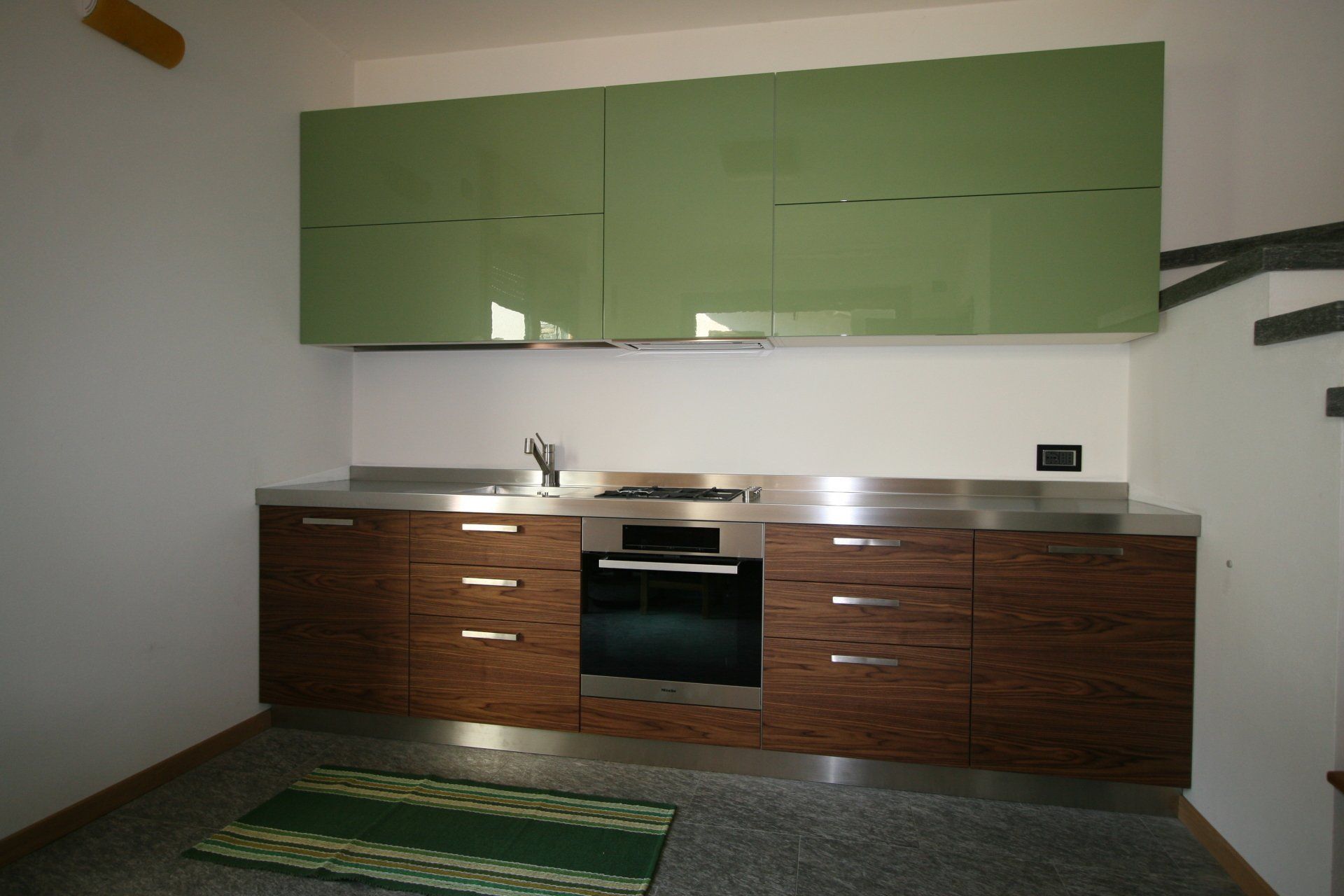 Cucina moderna con mobili verdi, basi in legno ed elettrodomestici in acciaio inossidabile.