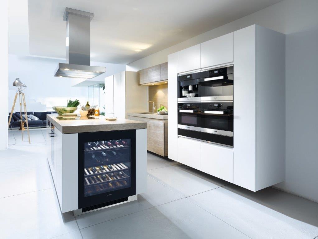 Cucina moderna bianca con isola, forni a incasso e cassetto cantinetta per vini.