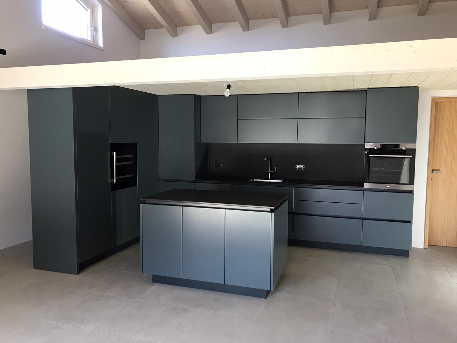Cucina moderna con mobili blu scuro, paraschizzi nero, isola e travi a vista sul soffitto.