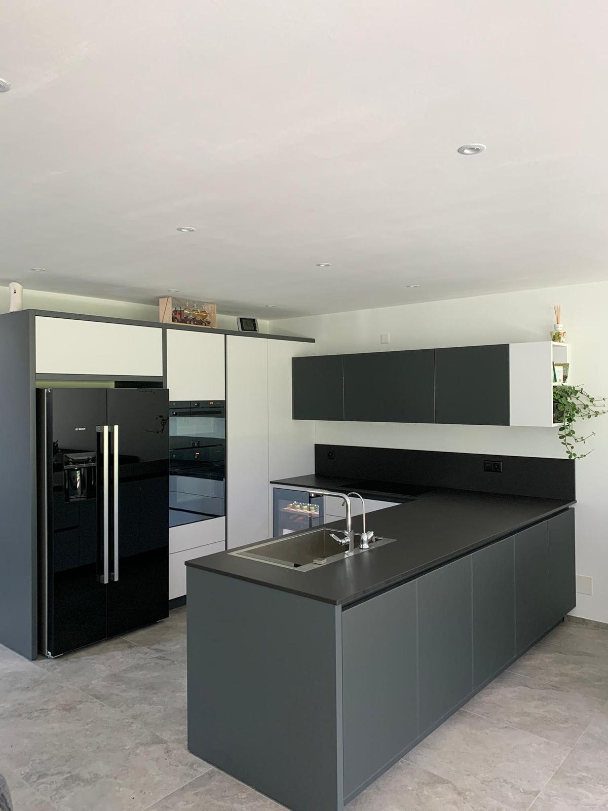 Cucina moderna grigia con isola nera, lavello in acciaio inox e frigorifero nero, vista da un'angolazione