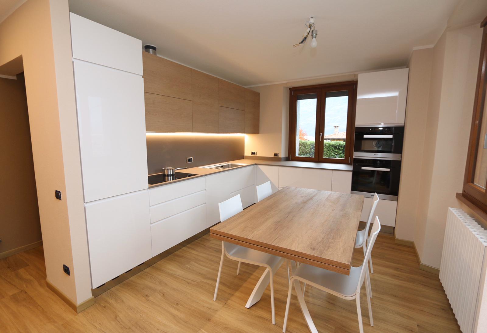 Cucina moderna con mobili bianchi, tavolo da pranzo in legno e sedie vicino a una finestra