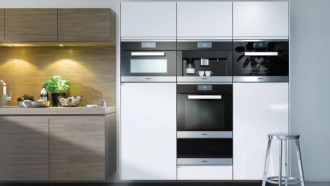 Cucina moderna con elettrodomestici a incasso, mobili in legno e bianchi e un piccolo sgabello sulla destra.