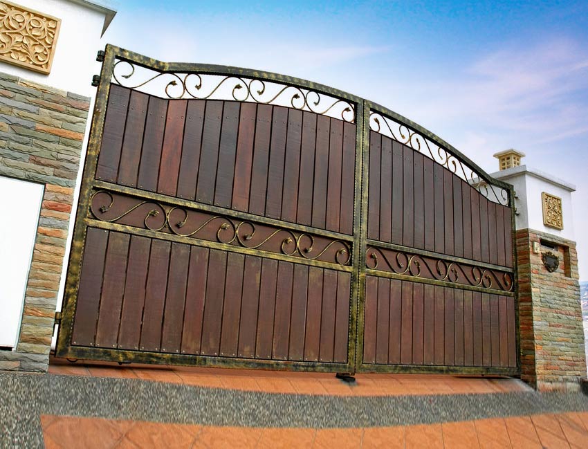 A wooden gate with a wrought iron frame is sitting in front of a brick building.
