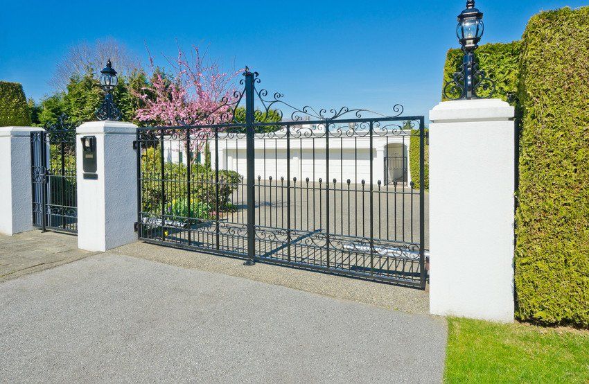 A wrought iron gate is surrounded by white pillars and trees.