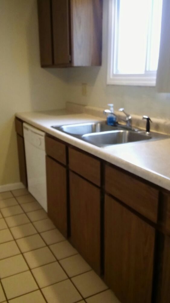 Kitchen with brown cabinets, white dishwasher, and double sink next to a window.