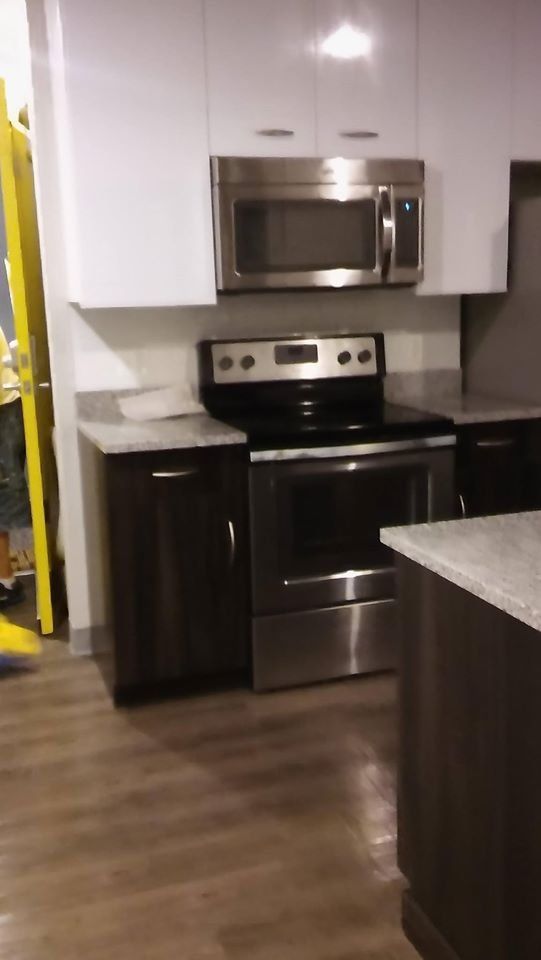 Modern kitchen with stainless steel appliances, dark cabinets, and white upper cabinets.