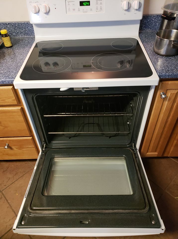 White electric stove with open oven door, inside light is on.