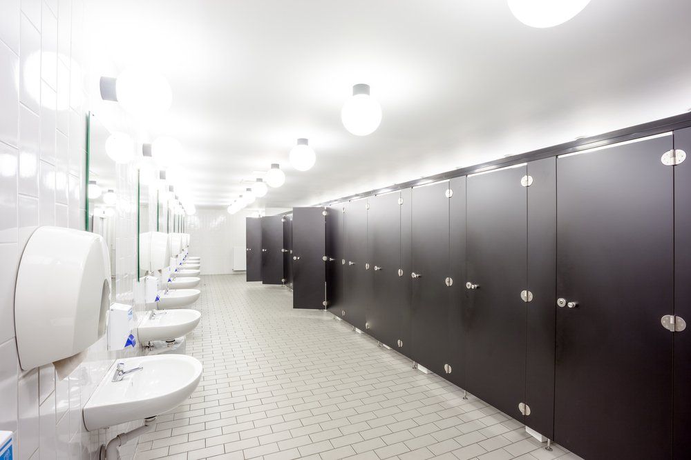 Public restroom with multiple stalls on the right, sinks and mirrors on the left, bright overhead lighting.