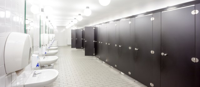 Public restroom with rows of stalls, sinks, and paper towel dispensers. White and black color scheme.