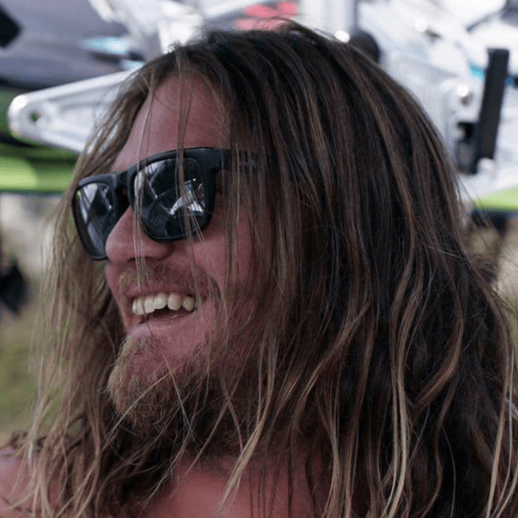 A man with long hair is wearing sunglasses and smiling