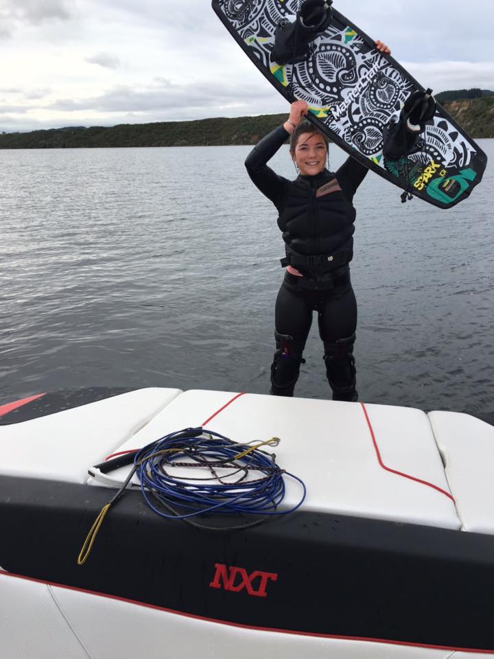 A person holding a surfboard on top of a boat that says nxt