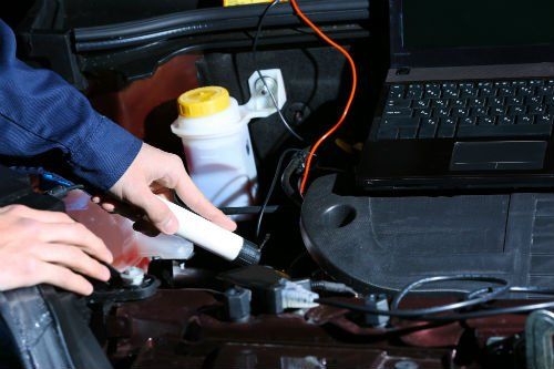 un meccanico che controlla il motore di un'auto e accanto un portatile appoggiato