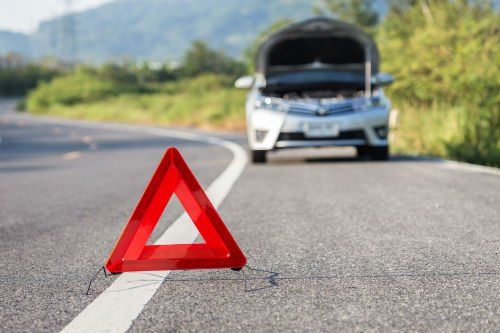 una macchina con il cofano aperto sulla strada con un triangolare rosso davanti