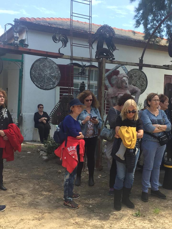 אנשים התאספו בחוץ ליד בניין, חלקם אוחזים בבגדים אדומים וצהובים, מתחת לפסלים תלויים.