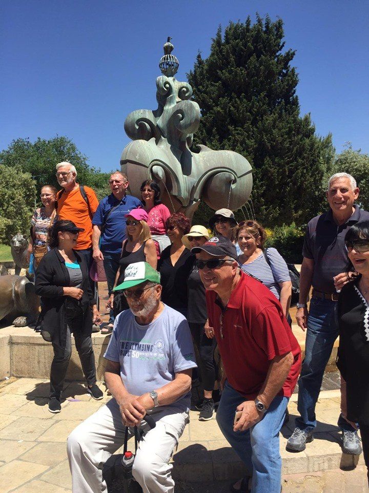 קבוצה פוזת מול פסל פיל גדול בפארק חיצוני, כשמאחוריהם עצים ומדרגות אבן