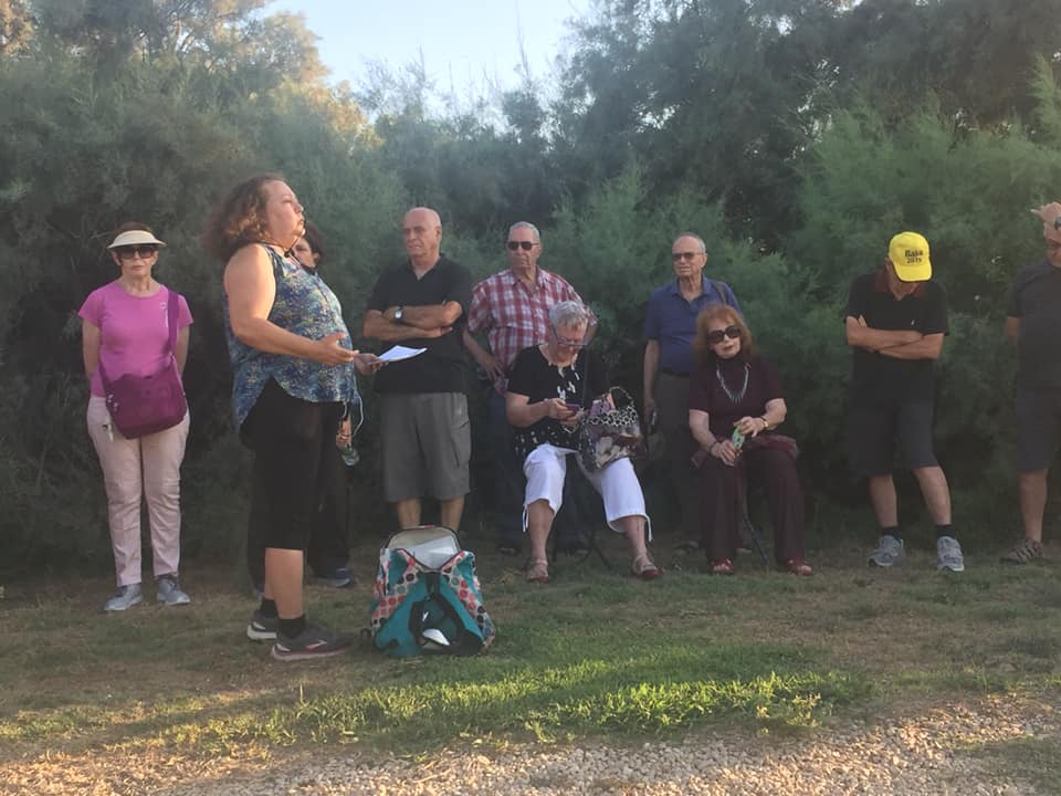 אנשים התאספו בחוץ בפארק, עומדים וישבים ליד עצים עם רדת החשיכה.