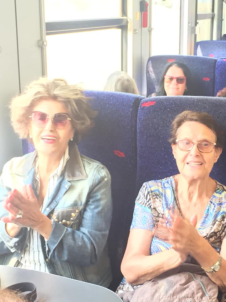 שני אנשים יושבים ברכבת, מוחאים כפיים ומחייכים ליד חלון.